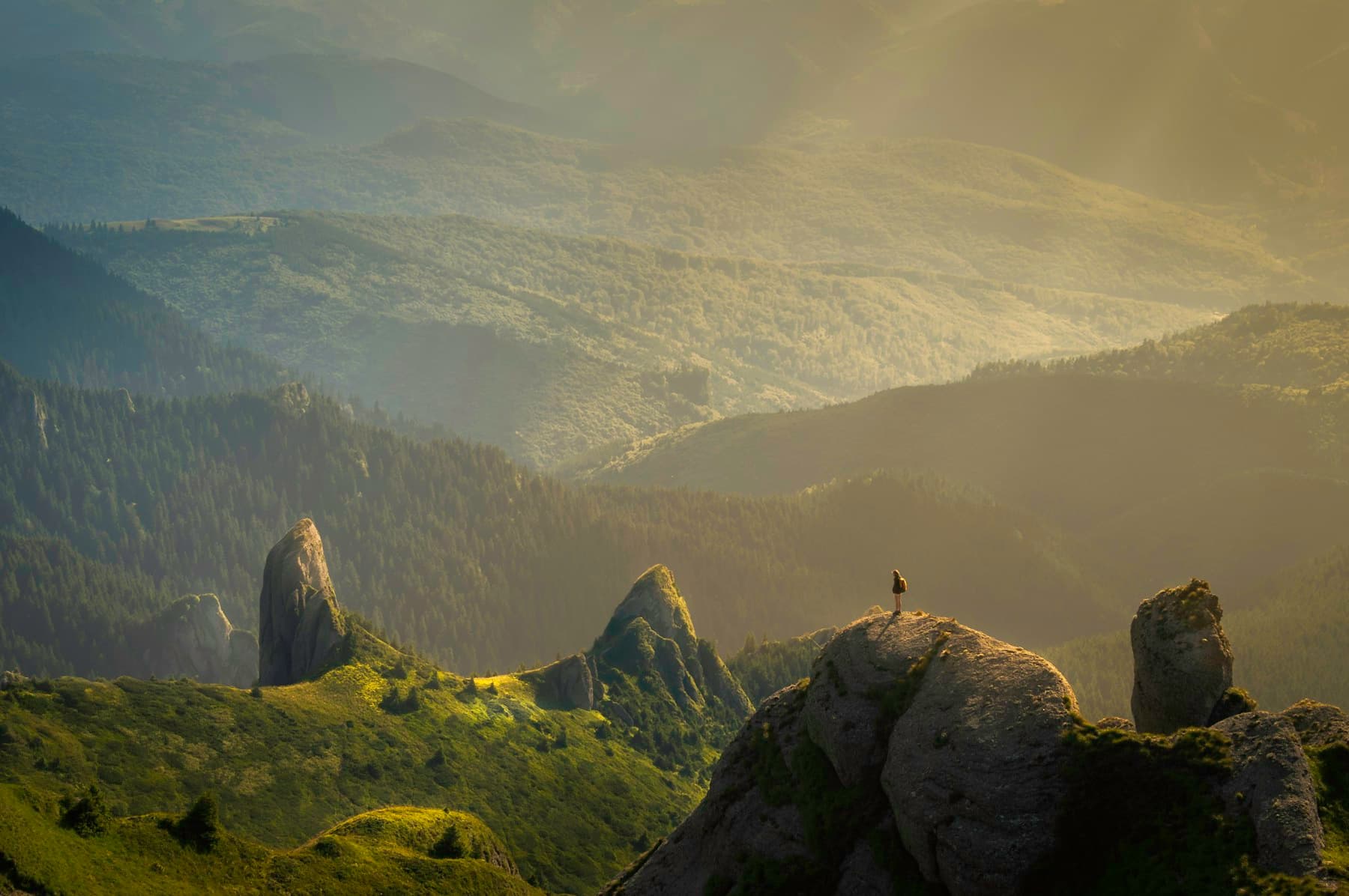 A lone traveler standing on a sunlit mountain ridge