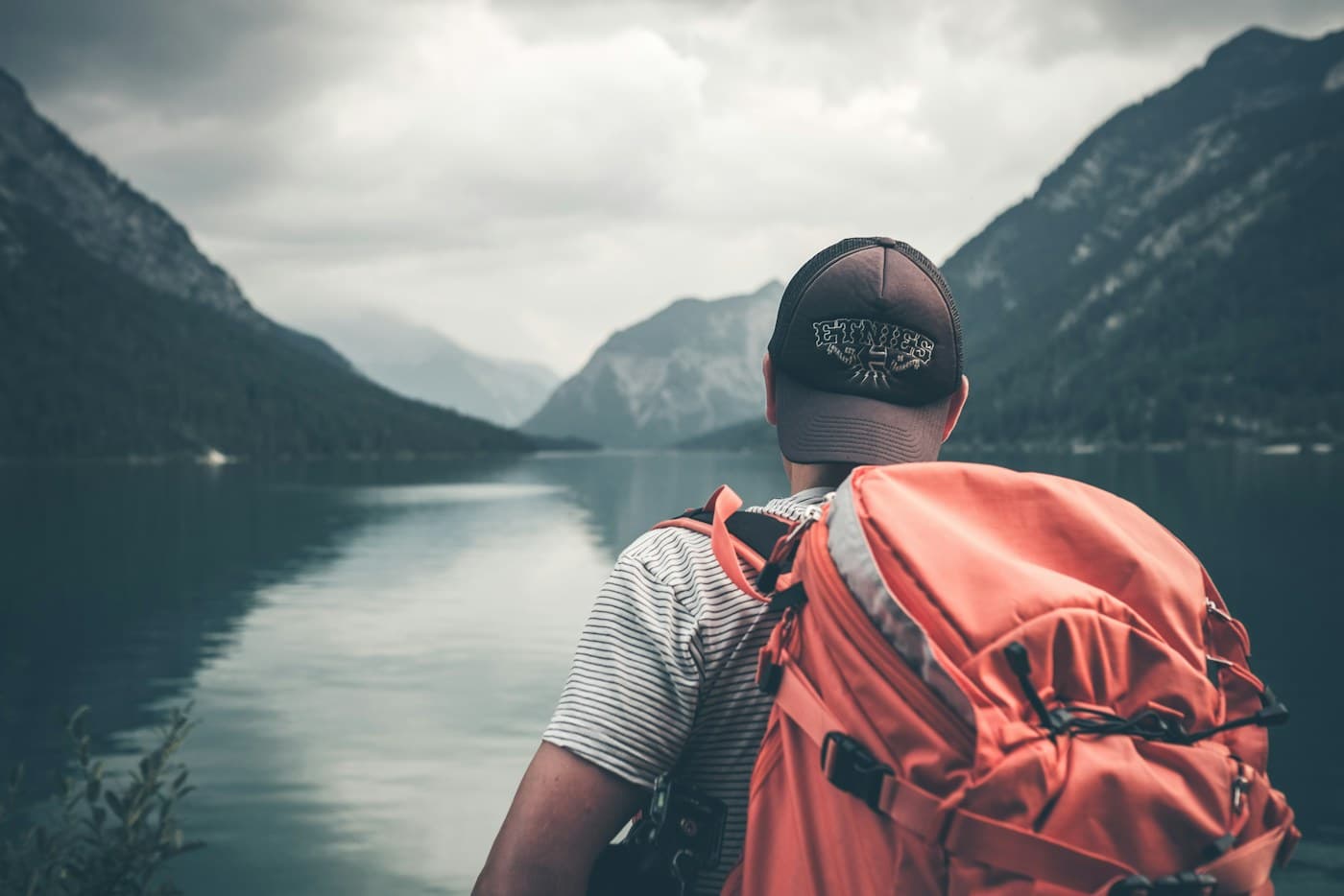 Traveler with a backpack looking toward an alpine lake